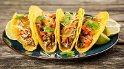 Four tacos, filled with succulent meat, fresh vegetables and other seasonings are sitting on a plate in a restaurant.