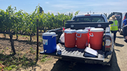 A flatbed truck on a farmsite has many coolers full of water. Farmworkers are visible in the background.