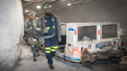 Two miners in protective gear walk through an underground mine