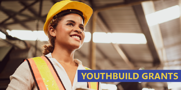 YouthBuild Grants. A young woman in hardhat and safety vest smiles at a construction site.