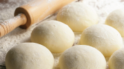 Balls of floured pizza dough rest on a kitchen surface near a rolling pin.