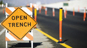 A sign that says open trench on a street in front of a construction site.