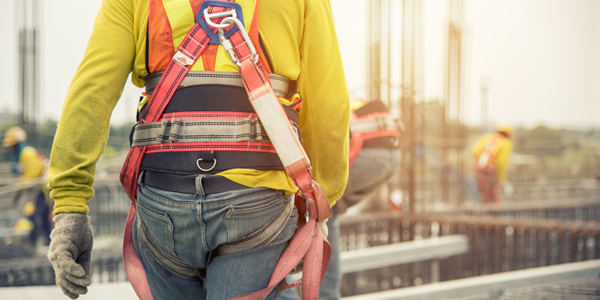 Several workers wearing fall harnesses, helmets and other safety gear on a construction site.