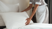 A hospitality professional plumps a pillow in a hotel room.