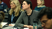 A woman with dark hair in a black and white jacket listens intently during a panel at the Global Forum on Migration and Development.