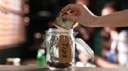 A person drops cash into a tip jar.