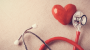 A red stethoscope lying next to a red heart.
