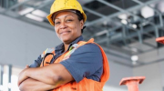 A woman in hardhat and safety vest poses with a confident expression.