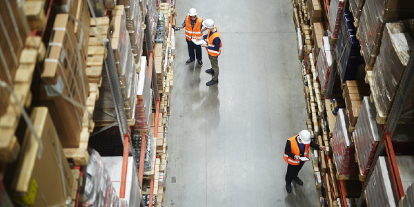 Aerial view of three workers in safety gear checking stock within a large warehouse.