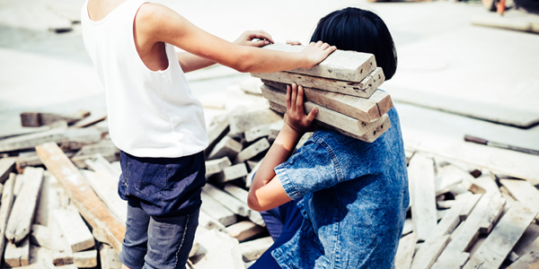 Two children, seen from behind, with piles of wood at a construction site.