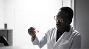 A Black scientist in a white lab coat examines a test tube.