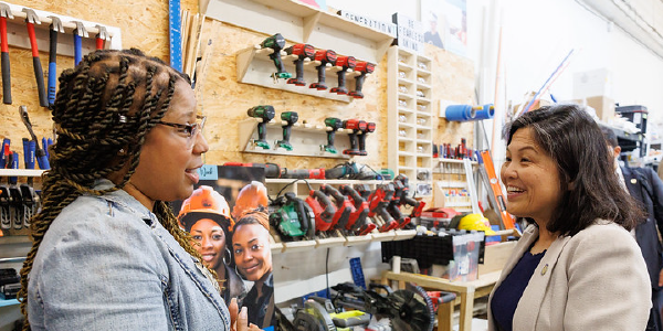 In front of a wall of hammers, drills and other tools, Acting Secretary Su chats with a young woman.