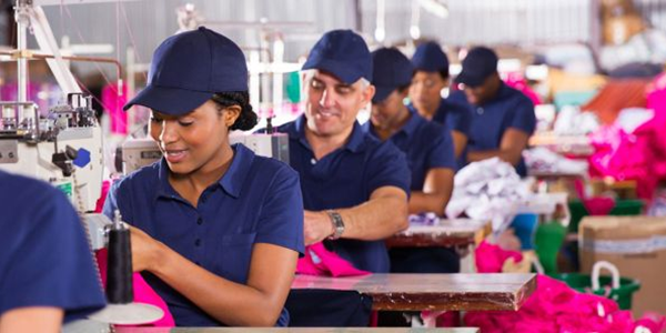 Workers wearing blue uniforms use sewing machines in a garment factory. 