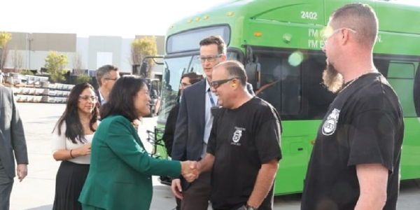 Acting Secretary Su shakes hands with workers while standing in front of an electric bus