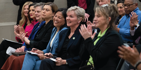 Acting Secretary Julie Su smiling while women alongside her applaud the speaker in front of them. 