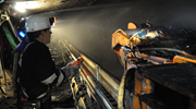 A coal miner wearing a helmet with a headlamp uses a remote control to direct a continuous mining machine underground.