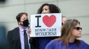 A woman holds a sign reading I heart home care workers.