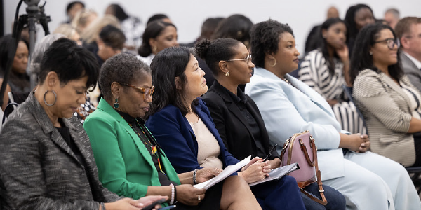 Surrounded by Black women leaders, Acting Secretary Su sits in an audience with her face turned toward an unseen speaker. 