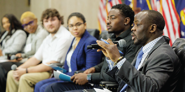 Deputy Assistant Secretary for Employment and Training Manny Lamarre speaks into a microphone while seated on a panel. Five young panelists listen attentively.