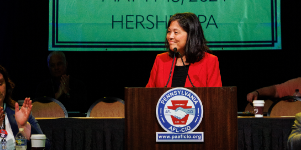 Acting Secretary Su smiles while standing behind a podium with a logo for the Pennsylvania AFL-CIO