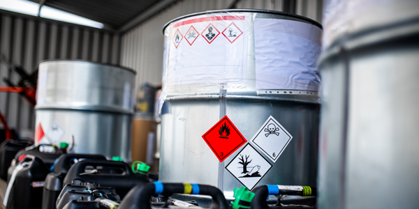 Several large barrels and smaller canisters in a warehouse with hazardous chemical labels.