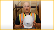 A man in safety glasses and safety vest holds a hardhat with the OSHA logo.