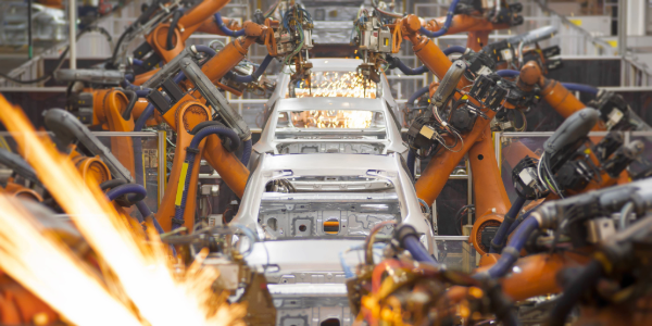Robotic arms actively assembling a car on the production line in an automobile factory. 