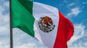 The flag of Mexico against a blue sky with clouds. 