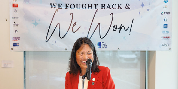 Acting Secretary Su smiles at a podium in front of a sign reading “We fought back and we won!”