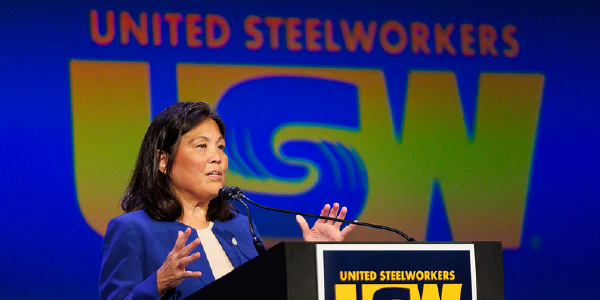 Acting Secretary Su speaks at a podium. Behind her is projected the United Steelworkers logo. 