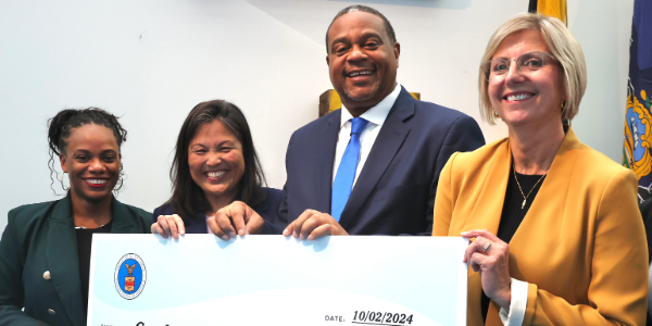 Four adults smile for a photo, holding a large novelty check