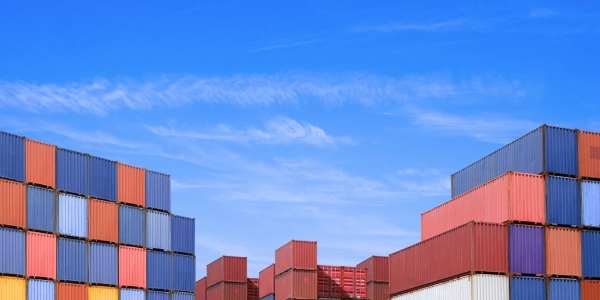 Shipping containers stacked at a port under a blue sky. 