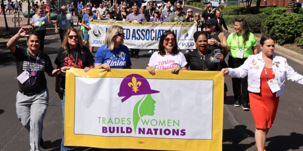 Acting Secretary Su carries a banner that reads “Tradeswomen build nations,” walking with other women down a New Orleans street.  