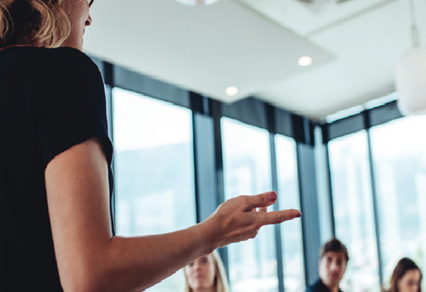Woman teaching business class with students around a table.