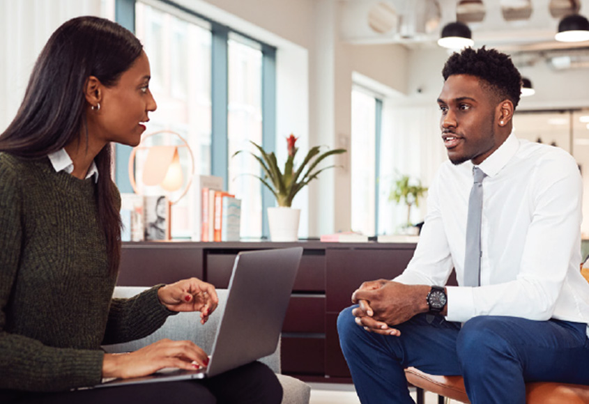 Woman with laptop talking with man in business office.