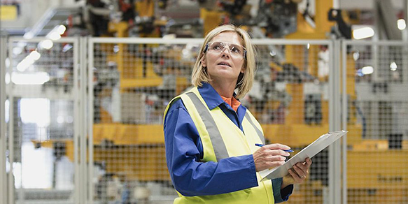 Woman wearing a yellow safety vest while holding a clipboard and inspecting a warehouse