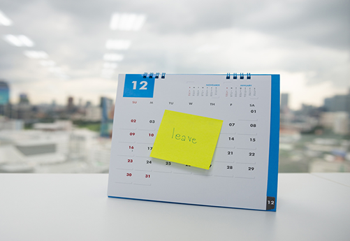 Desk calendar with yellow sticky note reading “leave” on the middle of the page