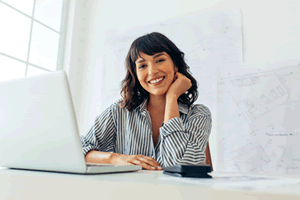 A woman smiles in front of an open laptop
