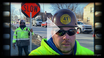 A screen shot of a video showing a union worker with a video play button in the middle.