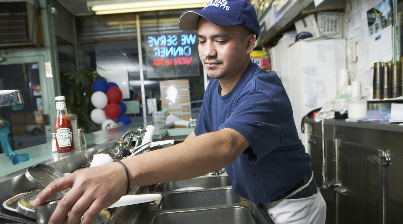 Un hombre lavando platos detrás del mostrador de una cafetería