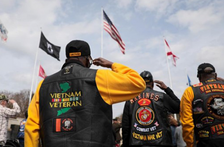 group of Vietnam Veterans saluting the U.S. flag. Several veterans have jackets on that say Vietnam Veteran on the back.